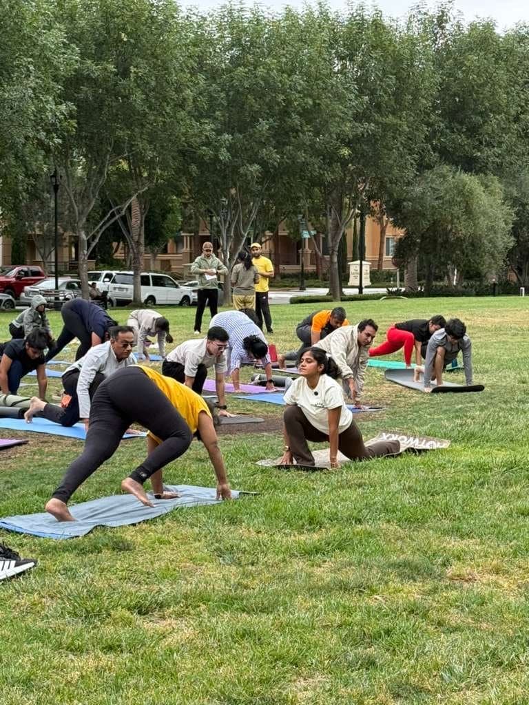 A group of students practising a low lunge on mats during an outdoor yoga class in a park, led by Kavya.